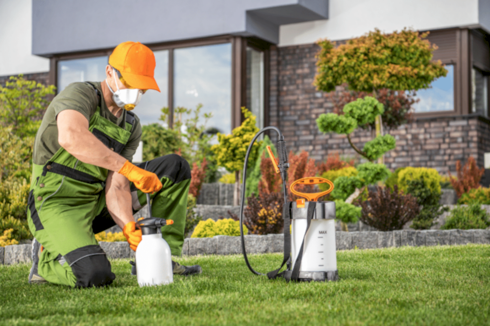 A man in green overalls and orange hat, performing pest control and landscaping services for a Meridian home.